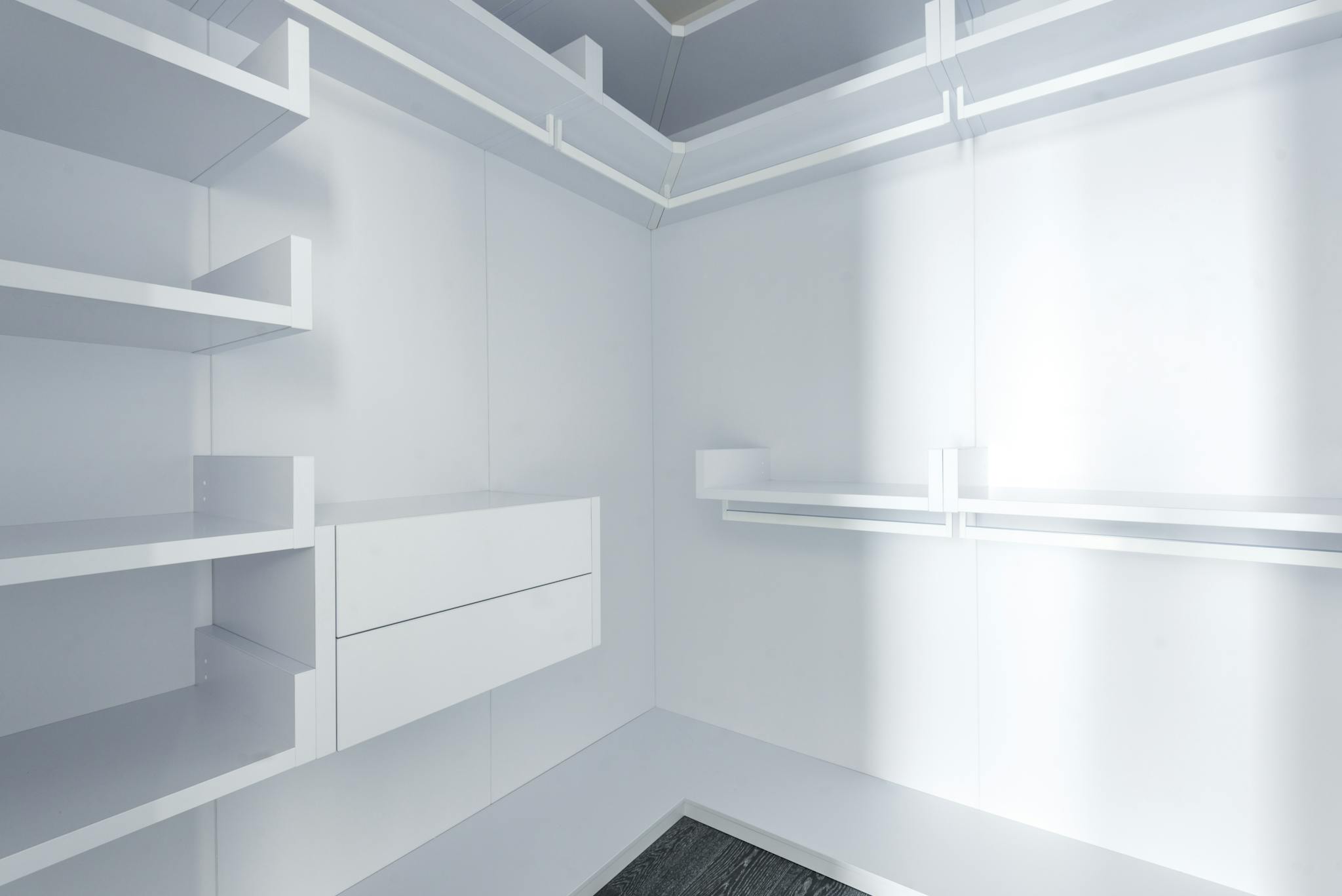 Modern minimalist walk-in closet with white shelves and bright lighting.